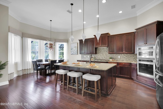 kitchen featuring dark hardwood / wood-style flooring, an island with sink, pendant lighting, light stone countertops, and backsplash