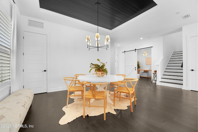 dining room with dark hardwood / wood-style flooring, a tray ceiling, a barn door, and an inviting chandelier