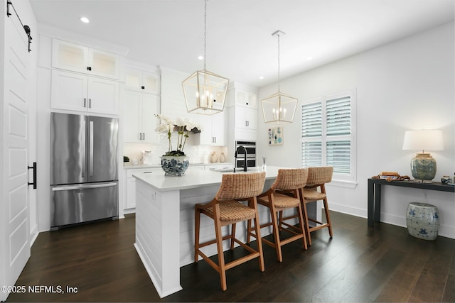 kitchen with stainless steel refrigerator, a kitchen island with sink, hanging light fixtures, white cabinets, and a barn door