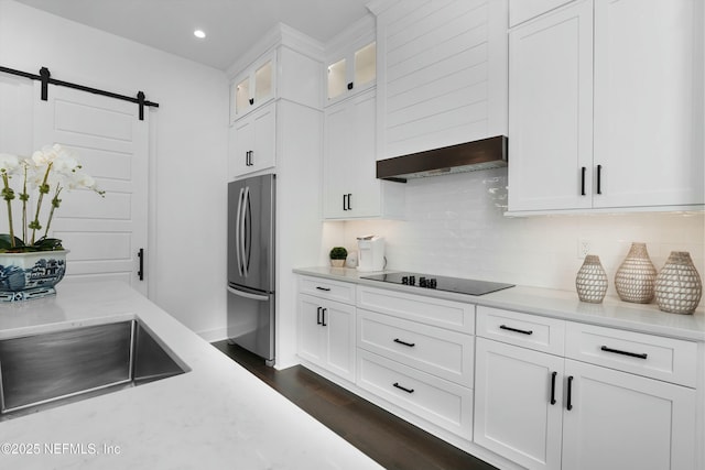 kitchen with black electric cooktop, stainless steel fridge, white cabinets, a barn door, and exhaust hood