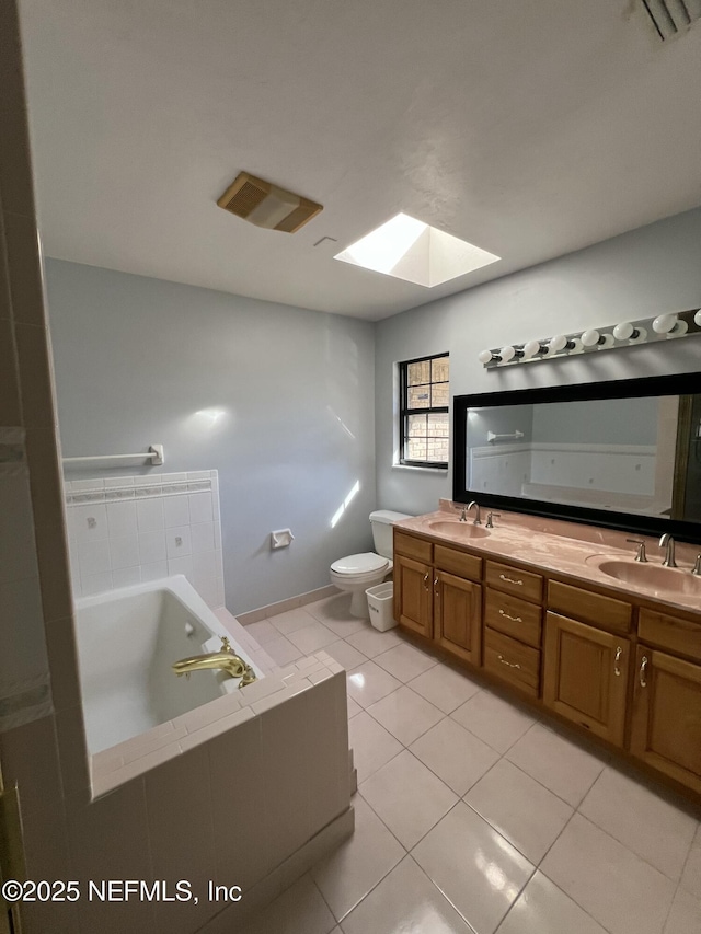 bathroom with a skylight, tiled bath, tile patterned flooring, vanity, and toilet