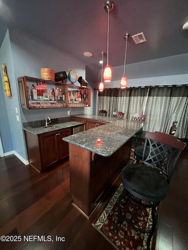 bar featuring sink, dark wood-type flooring, dishwasher, light stone counters, and decorative light fixtures