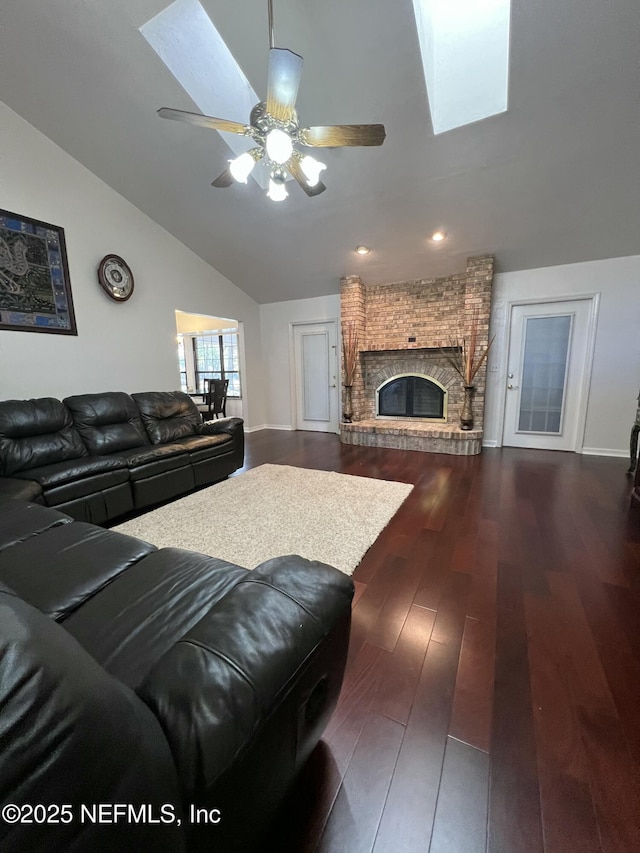 living room featuring lofted ceiling with skylight, a brick fireplace, dark wood-type flooring, and ceiling fan