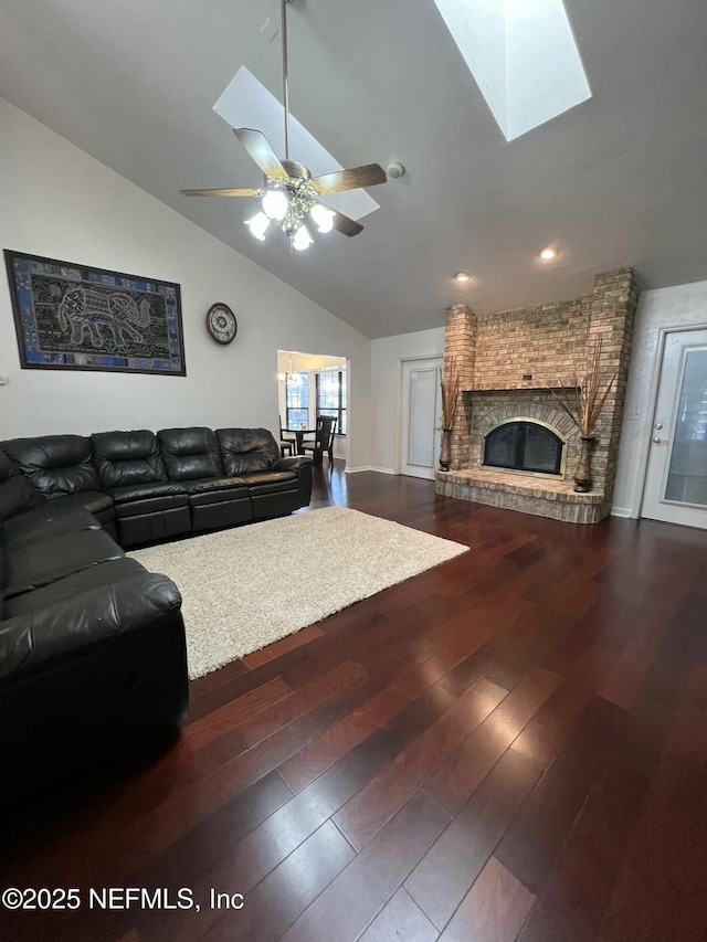 living room with wood-type flooring, vaulted ceiling with skylight, ceiling fan, and a fireplace