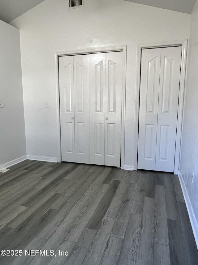 unfurnished bedroom with dark hardwood / wood-style flooring, vaulted ceiling, and multiple closets