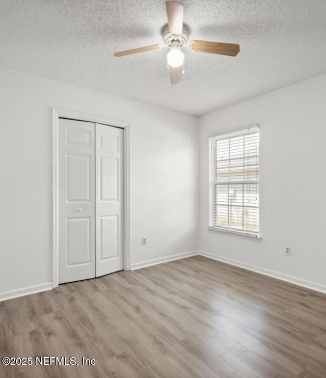 unfurnished bedroom with ceiling fan, light hardwood / wood-style floors, a closet, and a textured ceiling