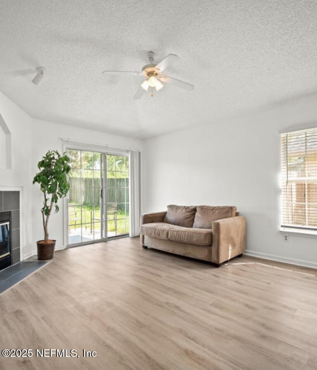 living room with a tiled fireplace, ceiling fan, a wealth of natural light, and light hardwood / wood-style floors