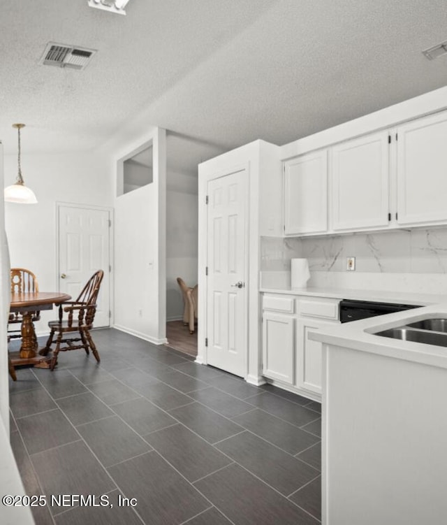 kitchen featuring pendant lighting, white cabinets, decorative backsplash, dark tile patterned floors, and a textured ceiling