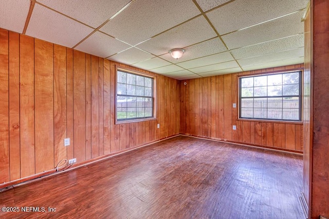 empty room featuring hardwood / wood-style flooring, a paneled ceiling, and wooden walls