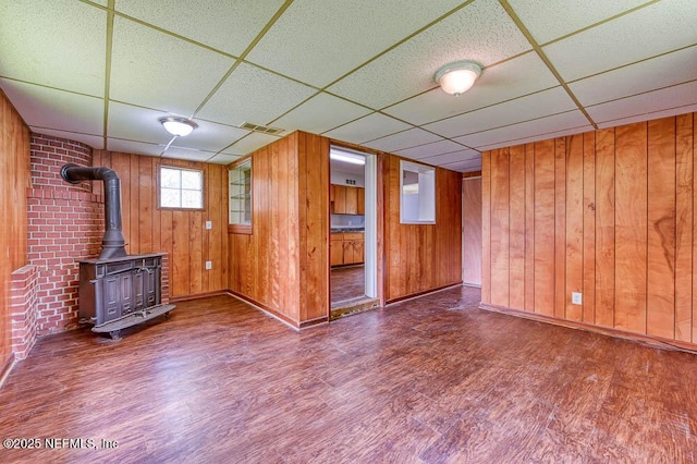 unfurnished living room featuring hardwood / wood-style flooring, a wood stove, a paneled ceiling, and wood walls