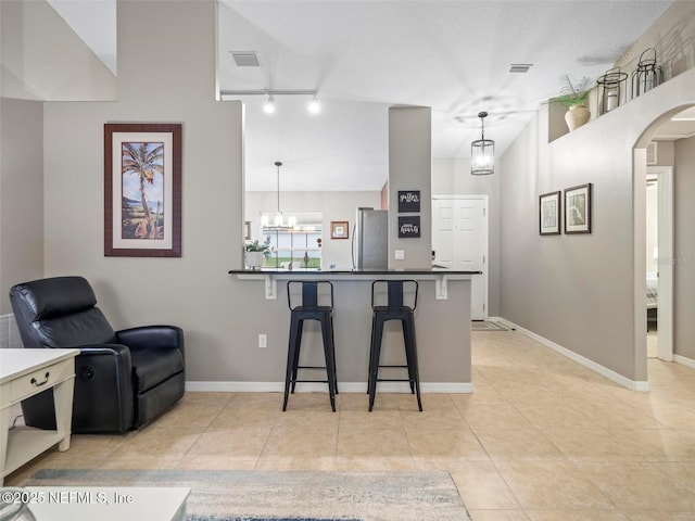 kitchen with light tile patterned floors, stainless steel fridge, hanging light fixtures, a kitchen breakfast bar, and kitchen peninsula