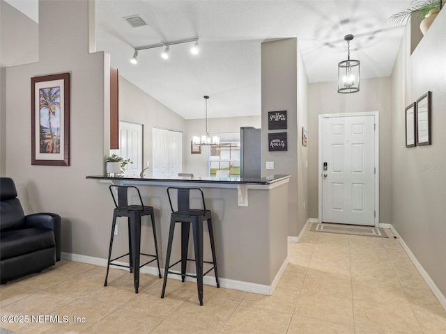 kitchen featuring stainless steel refrigerator, hanging light fixtures, a notable chandelier, a kitchen bar, and kitchen peninsula