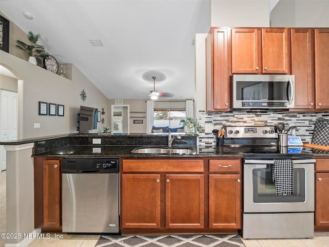 kitchen with sink, vaulted ceiling, dark stone countertops, stainless steel appliances, and decorative backsplash