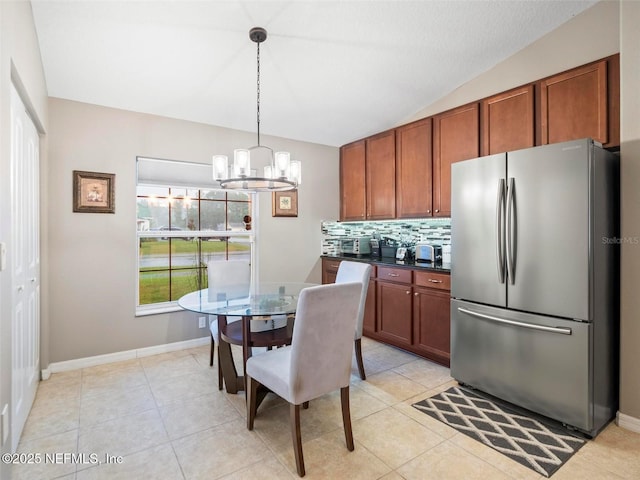 kitchen with vaulted ceiling, light tile patterned flooring, decorative light fixtures, tasteful backsplash, and stainless steel fridge