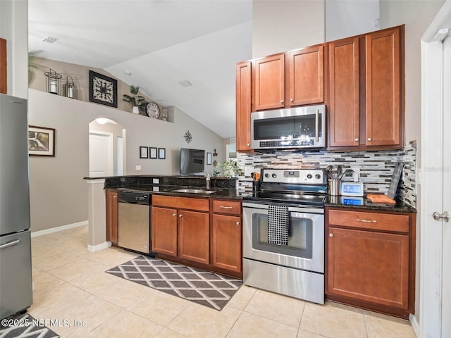 kitchen with sink, vaulted ceiling, dark stone counters, stainless steel appliances, and decorative backsplash