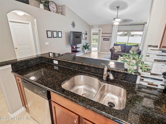 kitchen featuring lofted ceiling, sink, light tile patterned floors, dark stone countertops, and stainless steel dishwasher