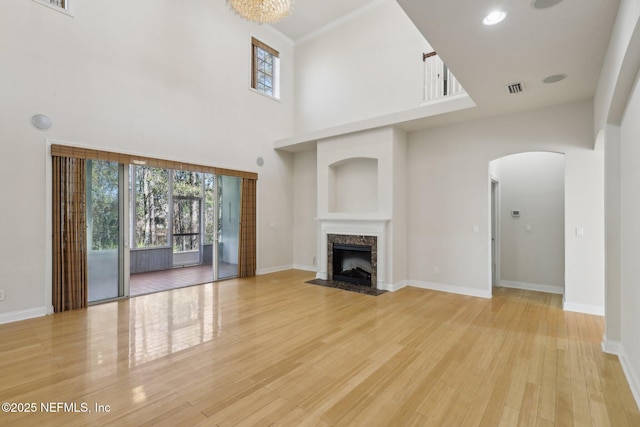 unfurnished living room featuring plenty of natural light, a high end fireplace, a towering ceiling, and light wood-type flooring