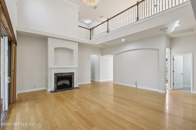 unfurnished living room with a towering ceiling, a high end fireplace, and light hardwood / wood-style flooring