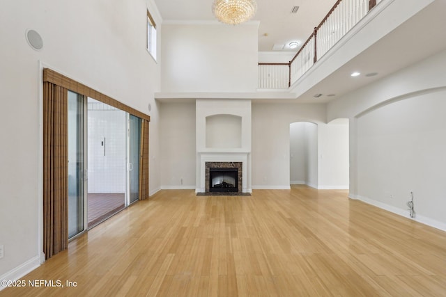 unfurnished living room featuring a towering ceiling, a fireplace, a chandelier, and light hardwood / wood-style floors