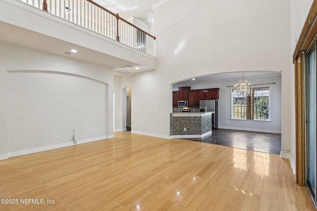 unfurnished living room featuring a towering ceiling, hardwood / wood-style floors, and a notable chandelier