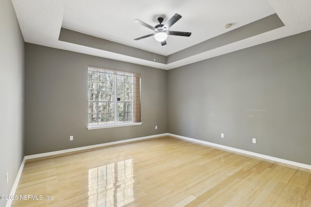 empty room with ceiling fan, a tray ceiling, and light hardwood / wood-style floors