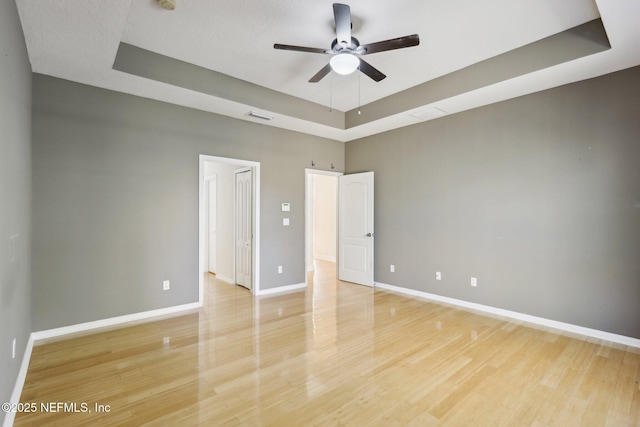 spare room featuring a raised ceiling, ceiling fan, and light hardwood / wood-style floors