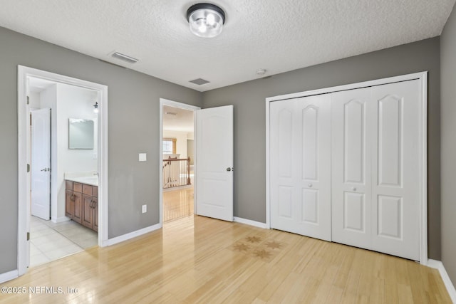 unfurnished bedroom with ensuite bath, light hardwood / wood-style floors, a closet, and a textured ceiling