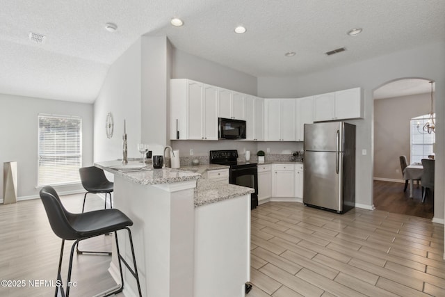 kitchen featuring light hardwood / wood-style flooring, white cabinetry, light stone countertops, black appliances, and kitchen peninsula