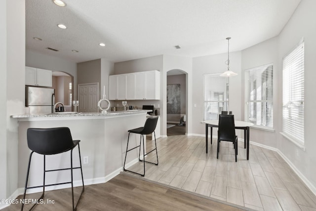 kitchen featuring a breakfast bar, stainless steel fridge, kitchen peninsula, pendant lighting, and white cabinets