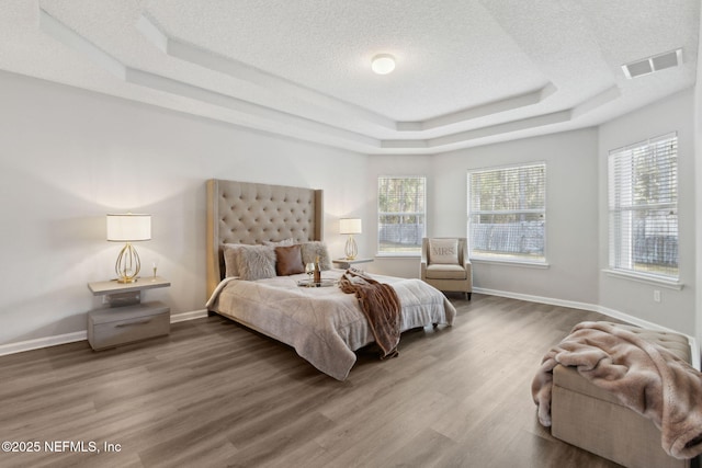 bedroom featuring wood-type flooring, a textured ceiling, and a tray ceiling