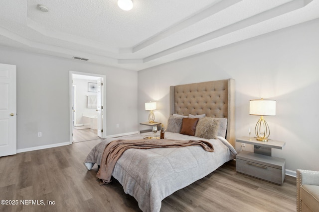 bedroom with a tray ceiling, wood-type flooring, a textured ceiling, and ensuite bathroom