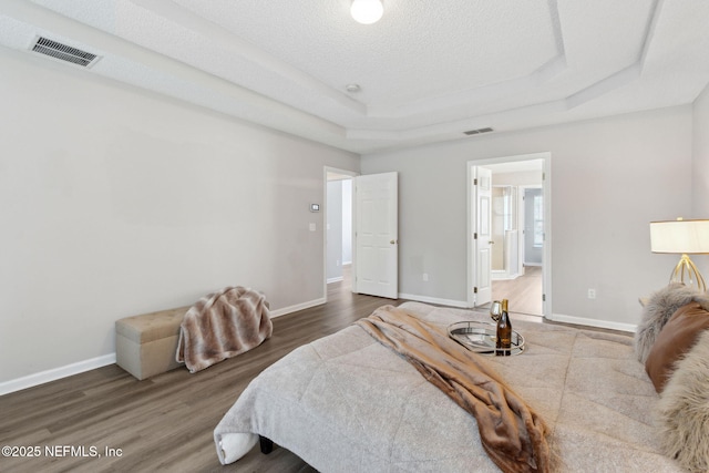 bedroom with a tray ceiling, hardwood / wood-style floors, and a textured ceiling