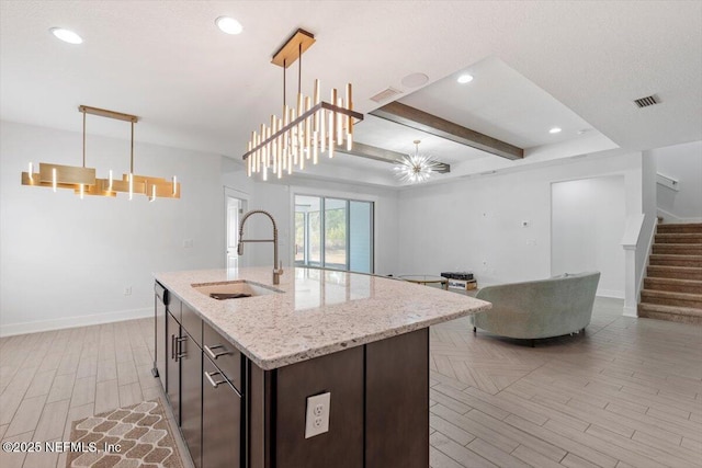 kitchen with a center island with sink, hanging light fixtures, sink, dark brown cabinets, and a chandelier