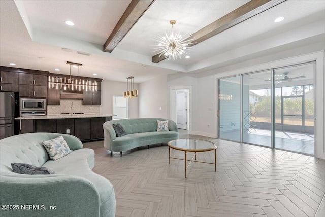 living room with light parquet flooring, a tray ceiling, beamed ceiling, sink, and an inviting chandelier