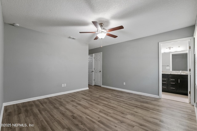 unfurnished bedroom featuring ensuite bath, sink, hardwood / wood-style floors, and a textured ceiling