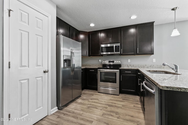 kitchen featuring sink, hanging light fixtures, stainless steel appliances, light stone countertops, and light hardwood / wood-style flooring