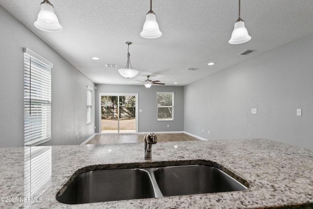 kitchen with pendant lighting, sink, light stone counters, and a textured ceiling