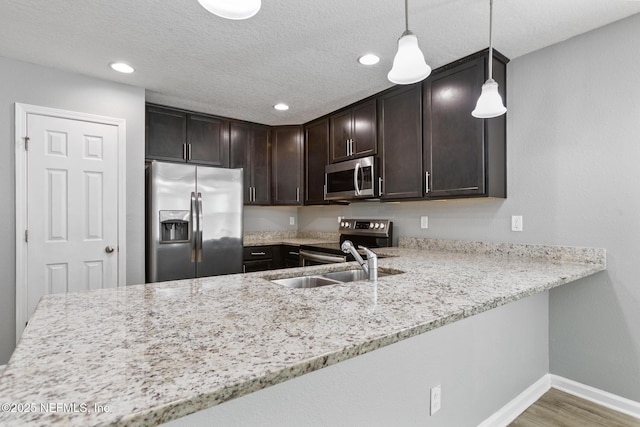 kitchen featuring dark brown cabinetry, sink, wood-type flooring, hanging light fixtures, and appliances with stainless steel finishes