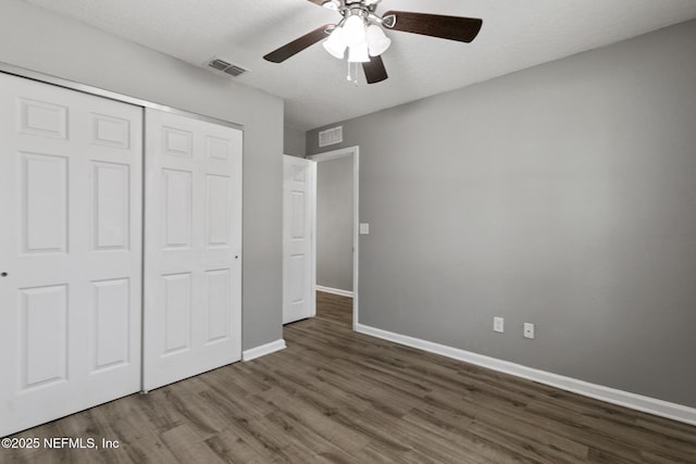 unfurnished bedroom with dark wood-type flooring, ceiling fan, a closet, and a textured ceiling