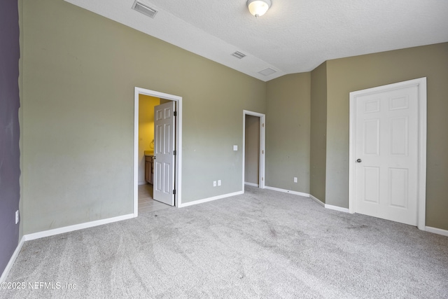 unfurnished bedroom featuring vaulted ceiling, light carpet, ensuite bathroom, and a textured ceiling