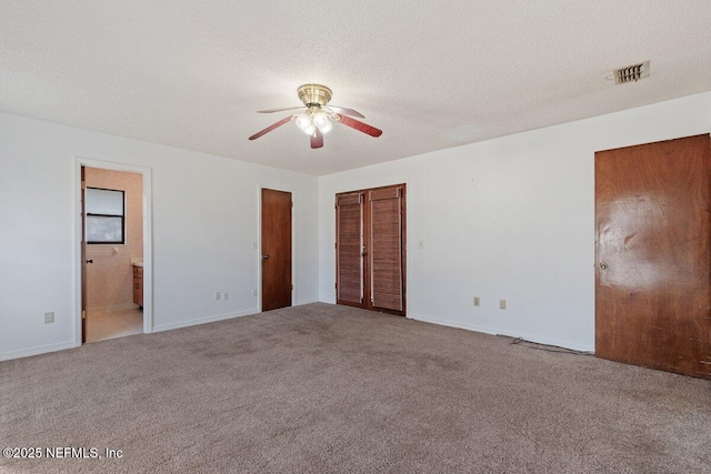 unfurnished bedroom with ceiling fan, ensuite bath, a textured ceiling, and carpet