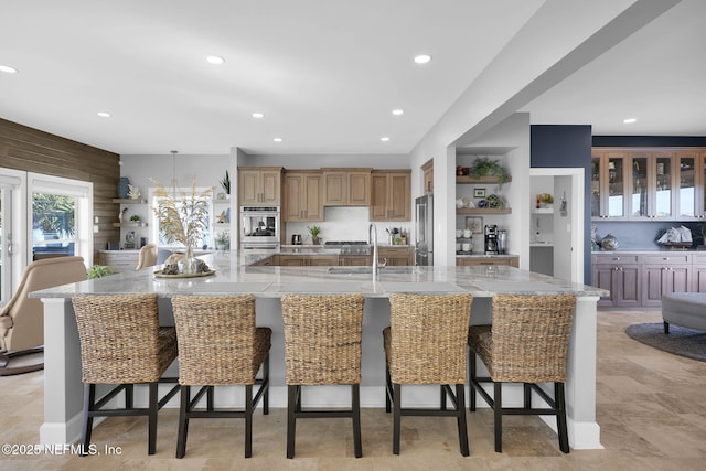 kitchen with sink, a breakfast bar, appliances with stainless steel finishes, light stone countertops, and a large island with sink