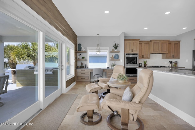 interior space with gas cooktop, double oven, built in desk, light stone countertops, and decorative light fixtures