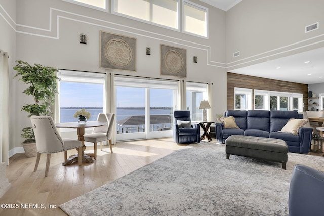 living room featuring a water view, a healthy amount of sunlight, light hardwood / wood-style floors, and a high ceiling