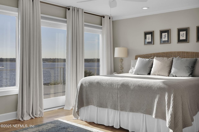 bedroom with crown molding, light wood-type flooring, and a water view