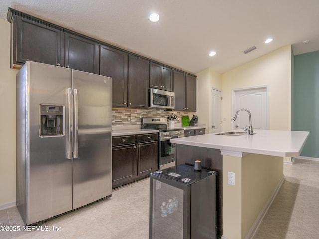 kitchen featuring sink, tasteful backsplash, dark brown cabinets, appliances with stainless steel finishes, and a kitchen island with sink