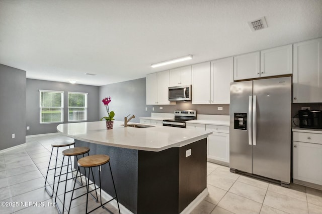 kitchen with sink, a kitchen island with sink, stainless steel appliances, white cabinets, and light tile patterned flooring