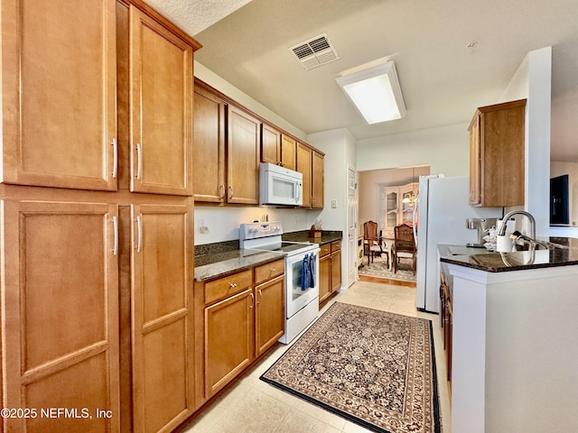 kitchen with light tile patterned flooring, white appliances, sink, and dark stone countertops