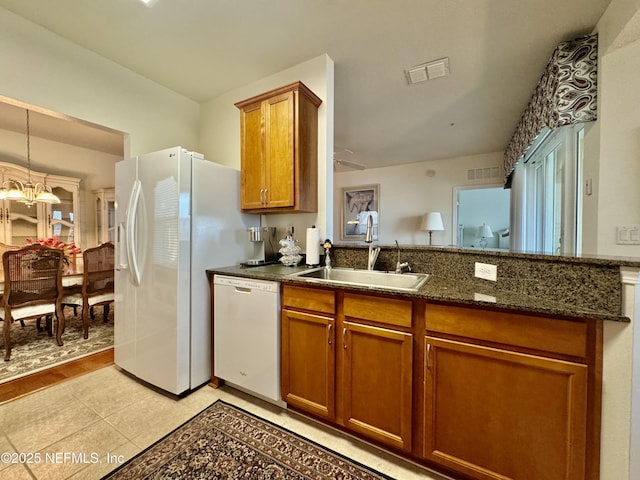 kitchen with pendant lighting, sink, dark stone countertops, white appliances, and an inviting chandelier