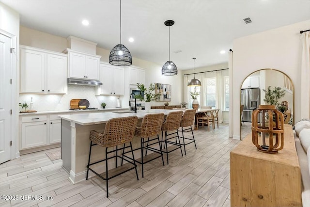 kitchen with white cabinetry, an island with sink, a breakfast bar area, hanging light fixtures, and stainless steel fridge with ice dispenser